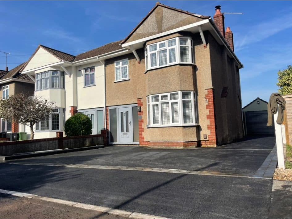 Finished full-width black tarmac driveway with a block-paved border at a pebbledash semi-detached house